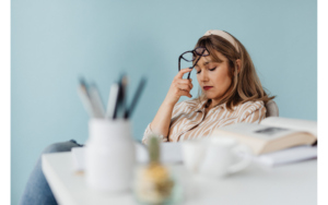 Woman holding glasses in her hand closing her eyes while pressing the glasses against her forehead