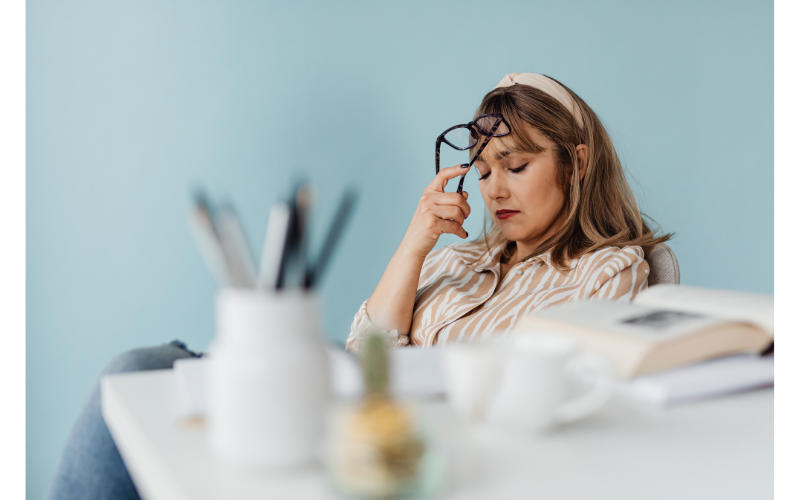 Woman holding glasses in her hand closing her eyes while pressing the glasses against her forehead